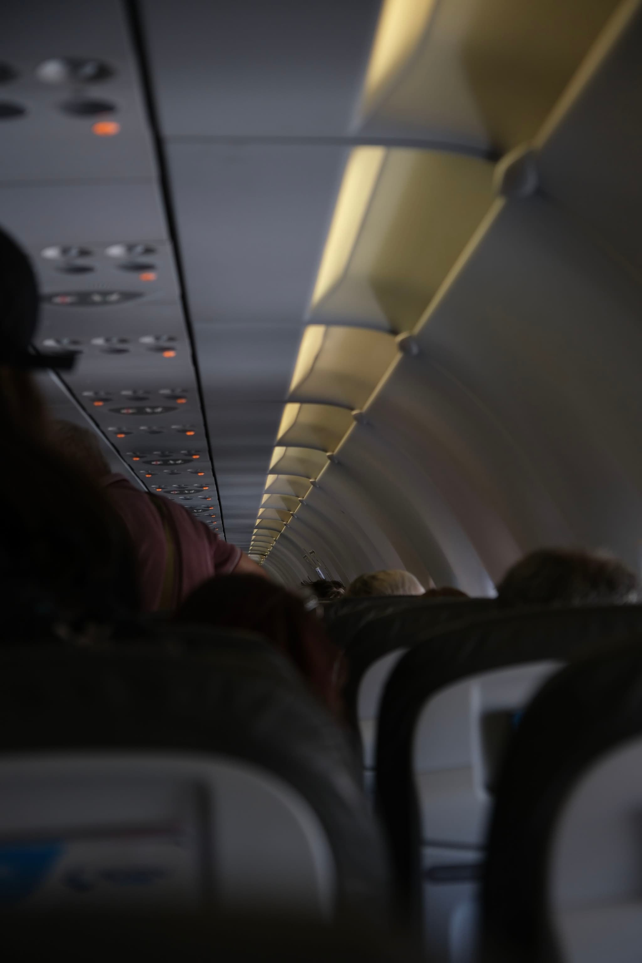 The interior of an airplane cabin with rows of seats and overhead compartments, viewed from the back