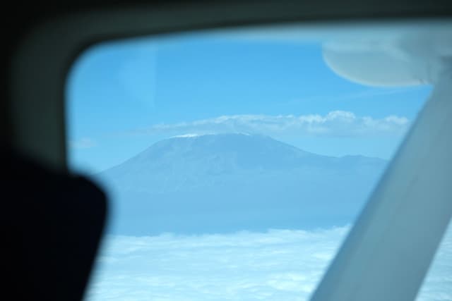 A view of a mountain peak surrounded by clouds, seen through an airplane window