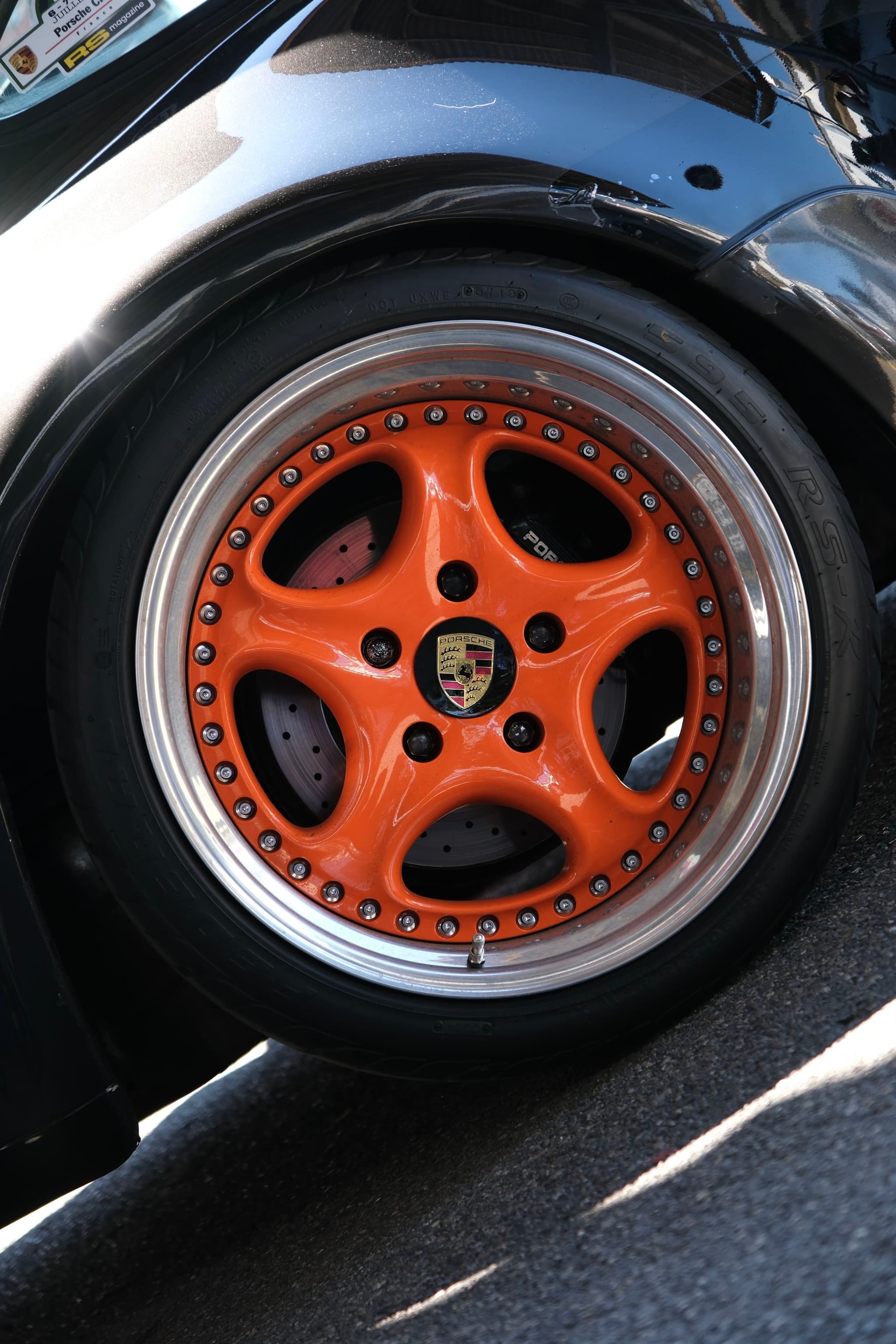 A close-up of a car wheel with an orange rim and a black tire, featuring a logo at the center