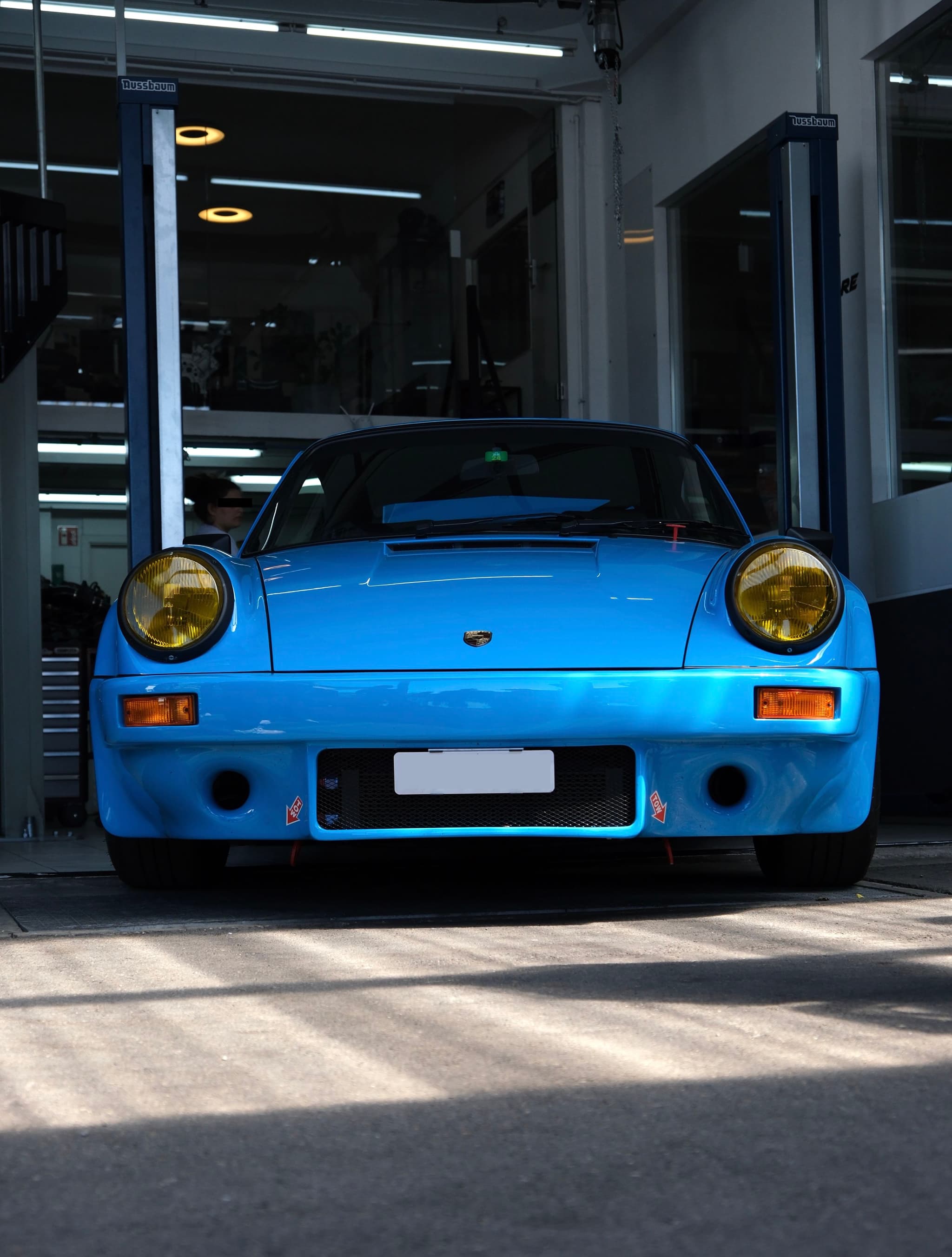 A blue sports car with yellow headlights is parked in a garage
