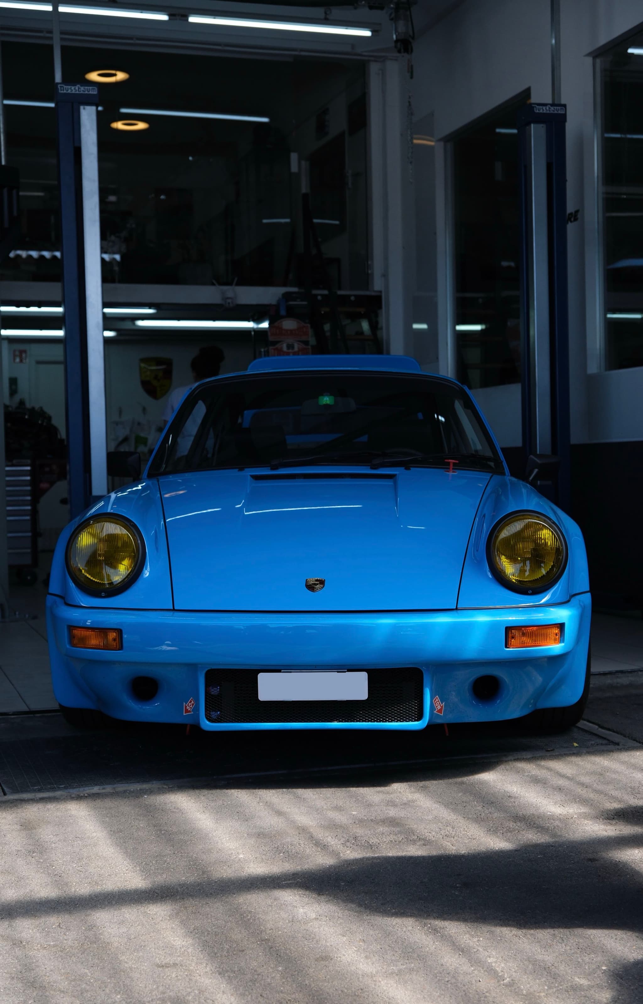 A blue sports car with yellow headlights is parked in a garage