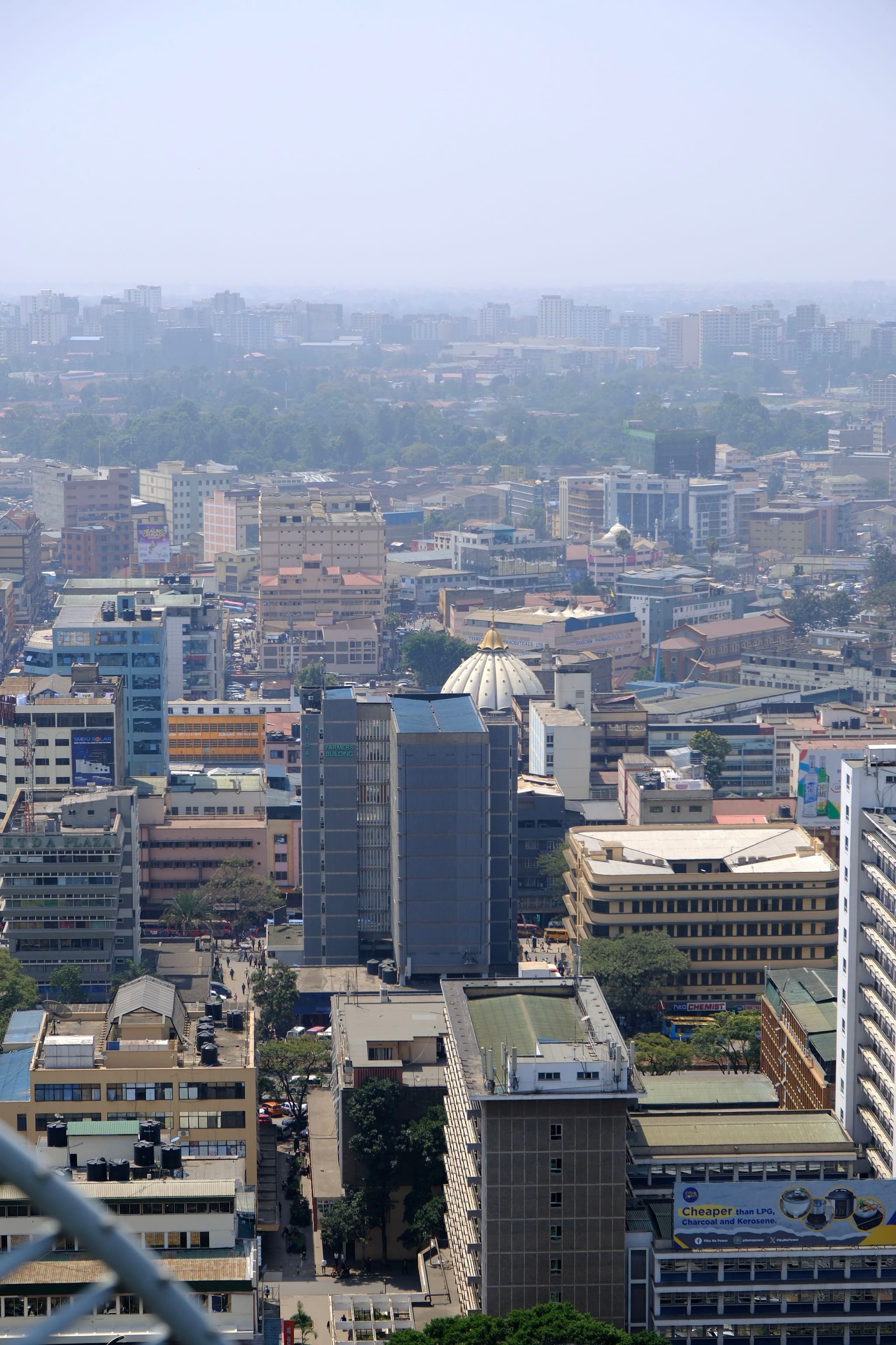 A cityscape with numerous buildings, including high-rises and a distinctive dome-shaped structure, under a hazy sky