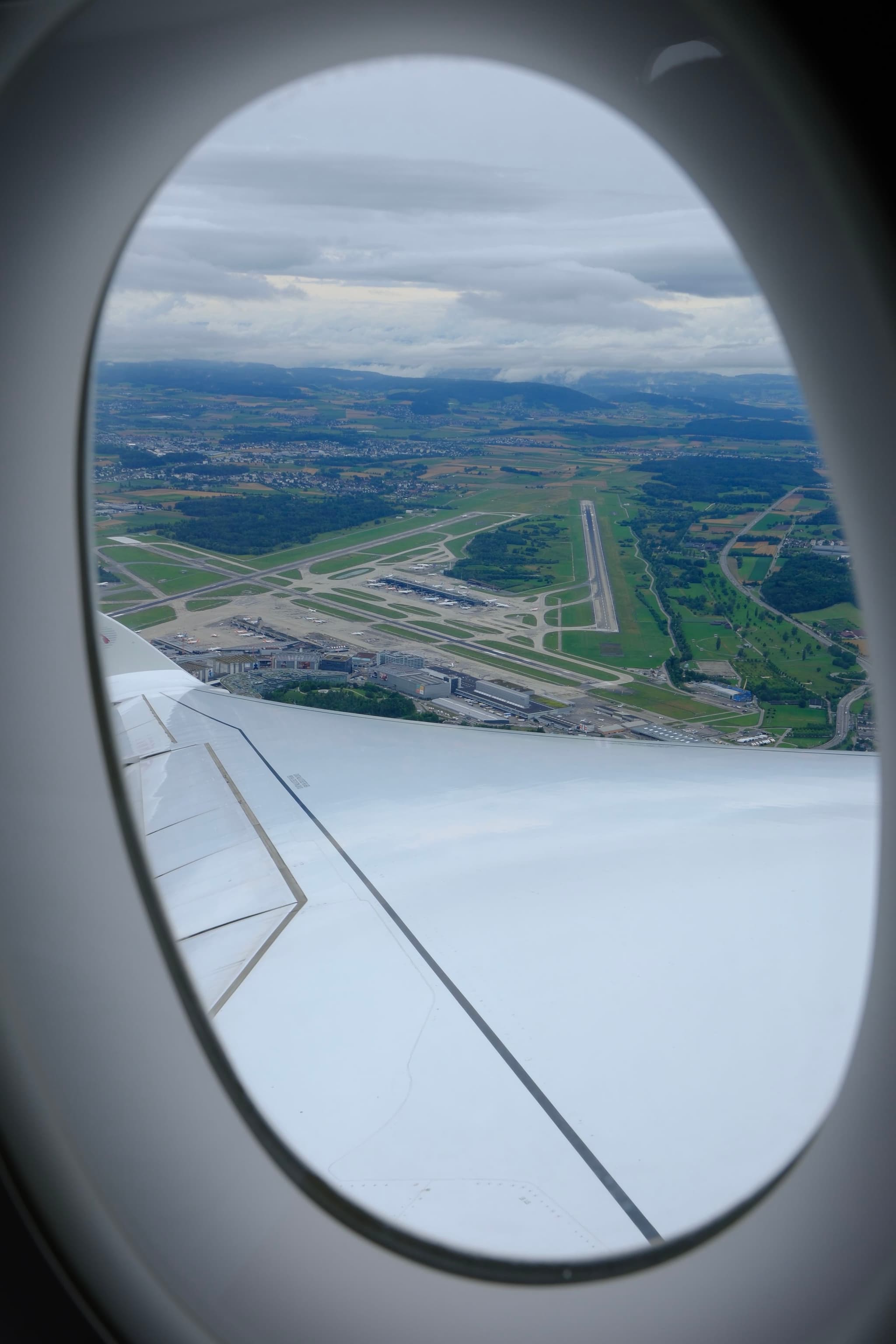 A view from an airplane window overlooking an airport runway and surrounding landscape