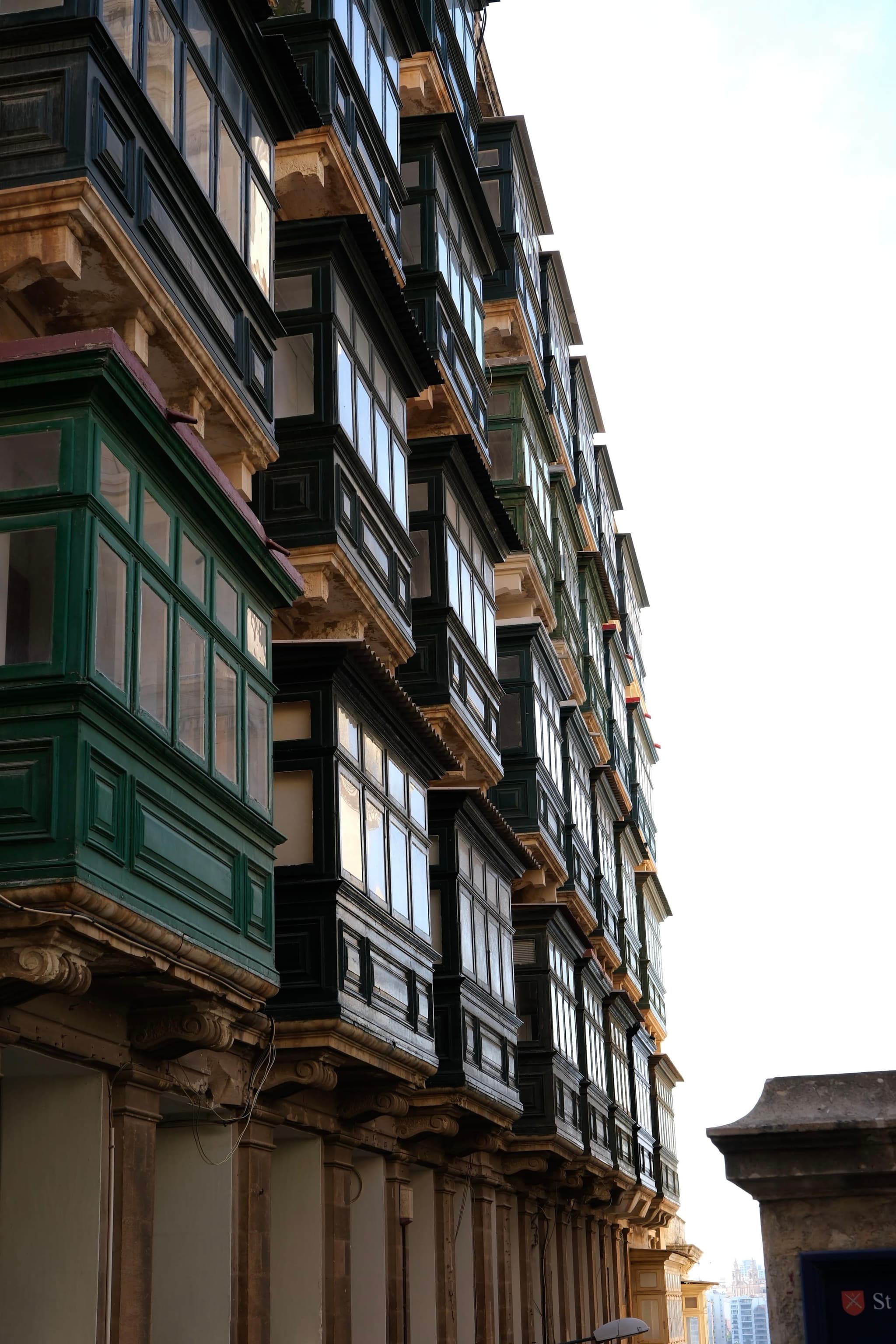 A building with multiple stories featuring traditional enclosed balconies, some painted green, against a bright sky