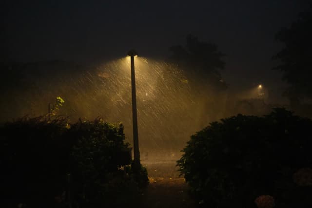 A streetlamp illuminates a misty street at night, casting a warm glow through the darkness and rain