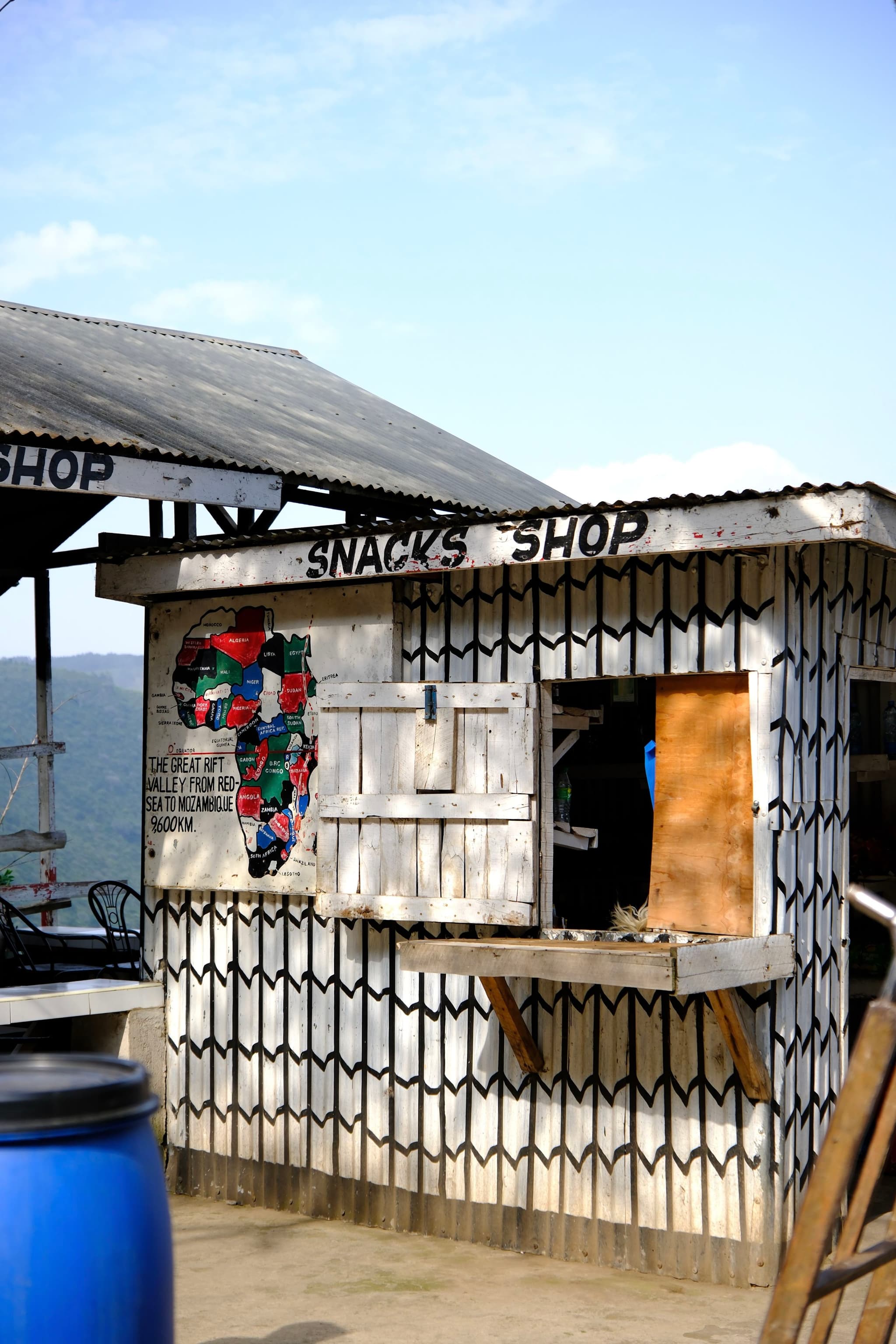 A small snack shop with a patterned exterior and a colorful map of Africa painted on the side. The shop has a wooden counter and is situated outdoors under a clear sky