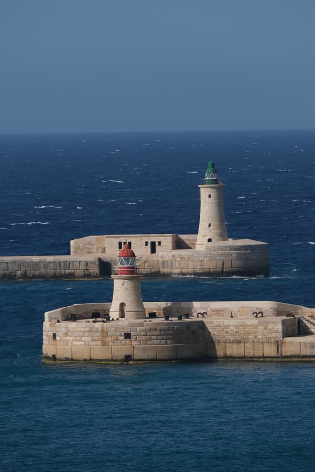 Two lighthouses on stone piers extend into a deep blue sea under a clear sky