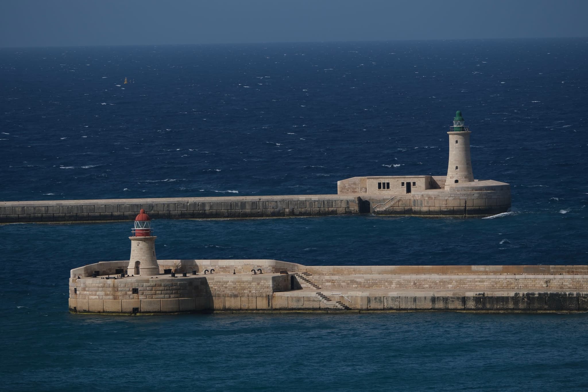 Two lighthouses on separate piers extending into a deep blue sea under a clear sky