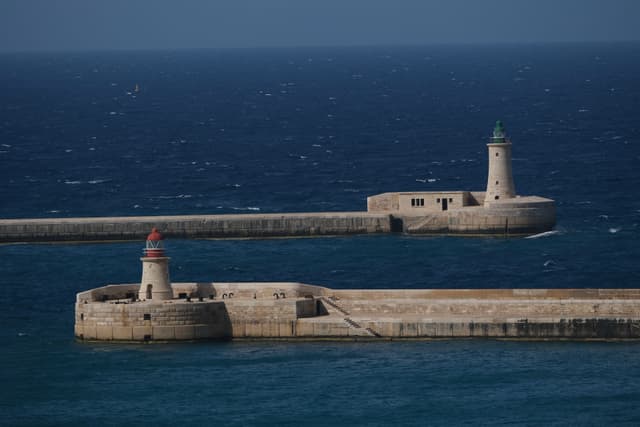 Two lighthouses on separate piers extending into a deep blue sea under a clear sky