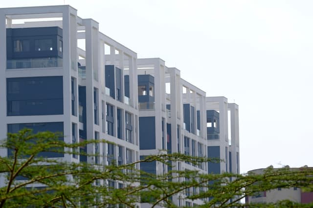 A row of modern, multi-story buildings with a geometric design, featuring large windows and surrounded by greenery